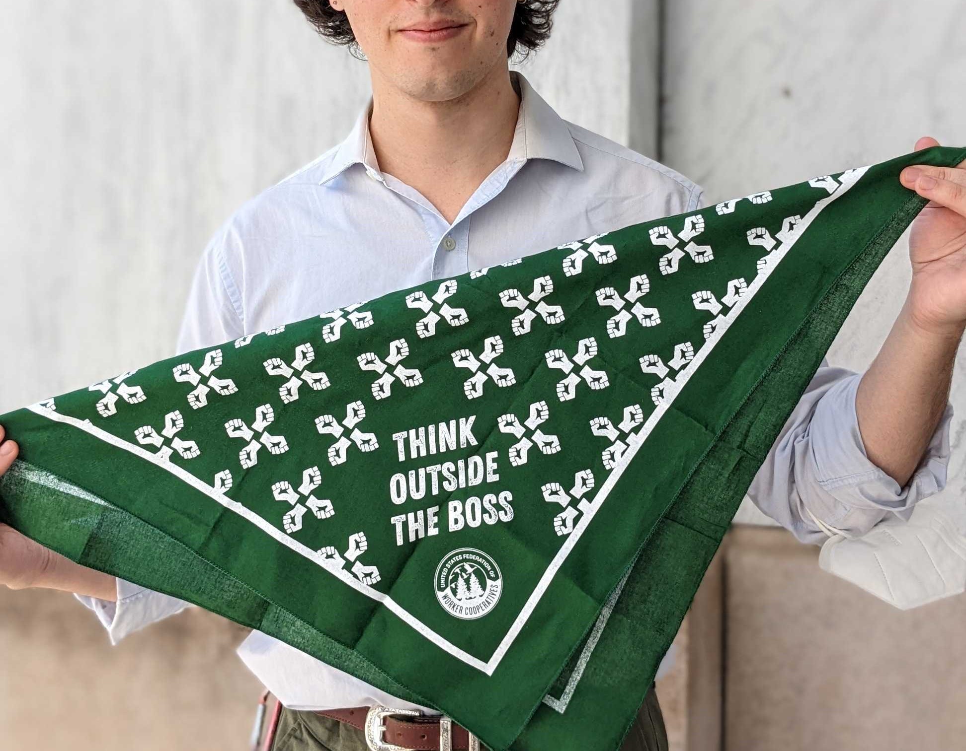 A picture of a person with a white collared shirt dark brown hair and blue eyes holding a dark green bandana that says "think outside the Boss"