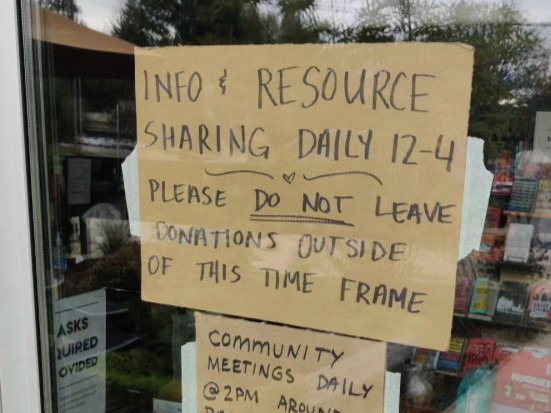 makeshift cardboard sign in storefront window that says "info and resource sharing daily 12 to 4. Community meetings daily at 2 pm around back"