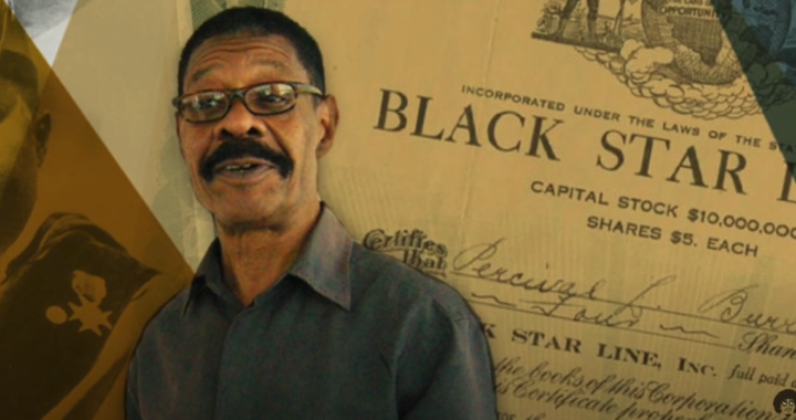 A photo of Clark Arrington who has brown skin, short hair, a mustache and eye glasses in front of some historical documents.